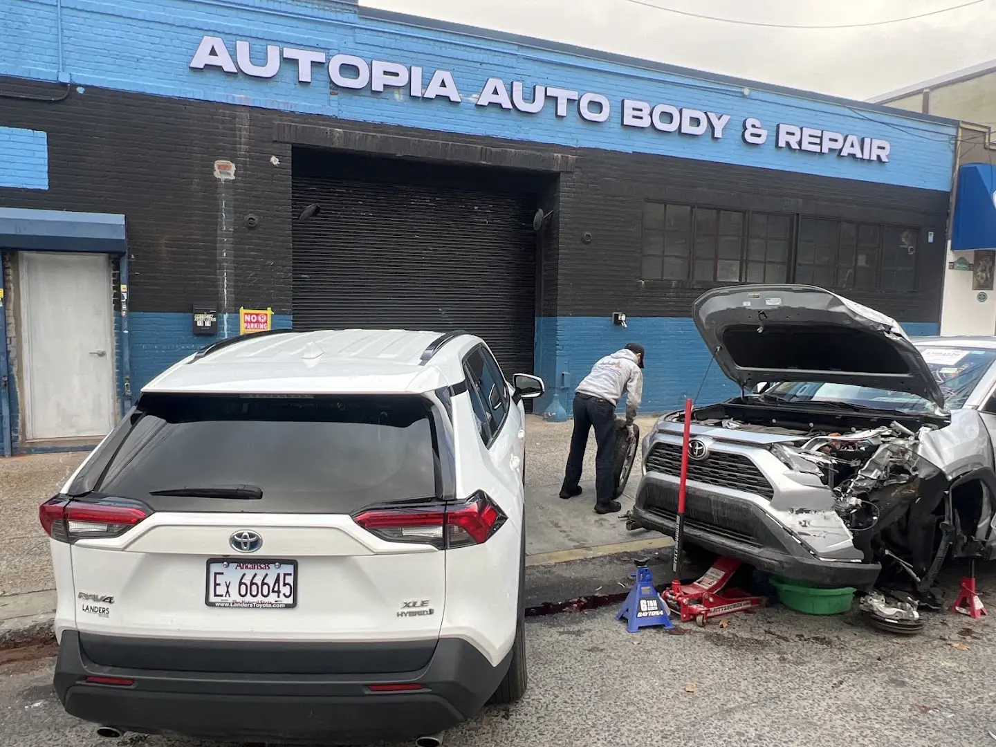 The Autopia Auto Body & Repair storefront on Steinway Street, with a technician working on a car outside the bay door