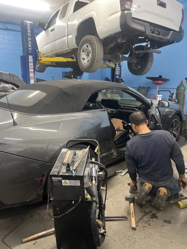 Inside the shop, a pickup on the lift and a technician working on a damaged convertible