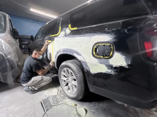 Technician sanding body filler along the rear panel of a black SUV