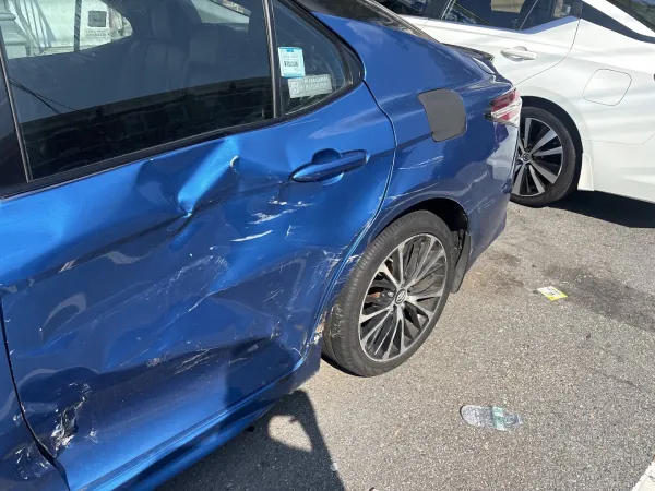 Blue sedan with a deeply dented rear door and quarter panel